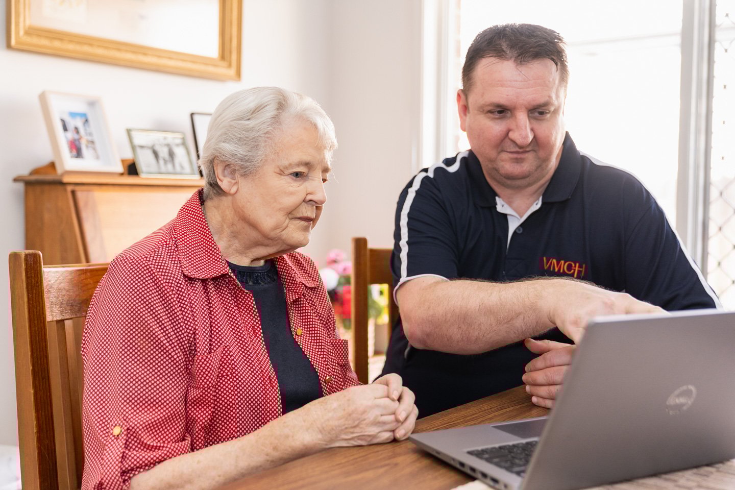 Elderly female sitting with a VMCH worker at a table, looking at a laptop