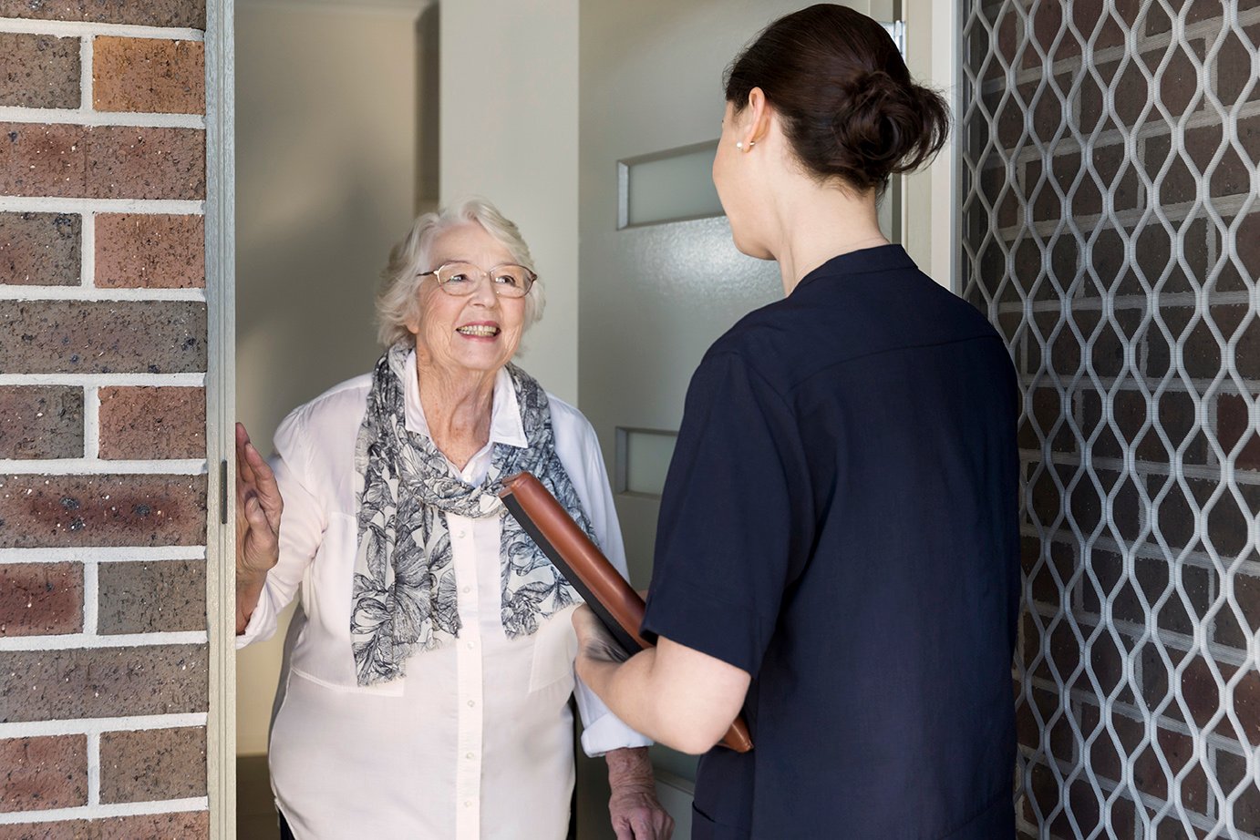 A woman visits an older lady at her front door to talk about exercise physiology