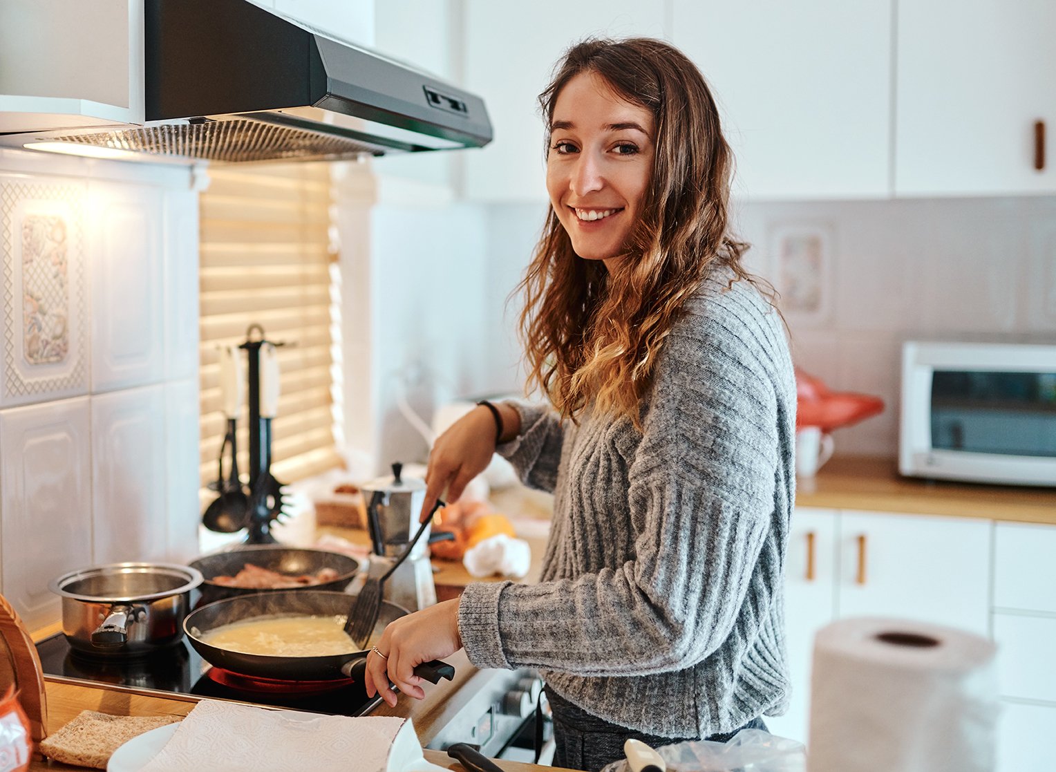Young female carer cooking a meal on the stove, smiling at the camera