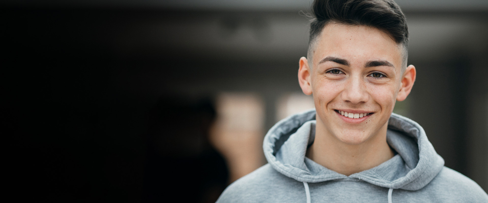 Adolescent boy smiling at camera wearing a grey hoodie