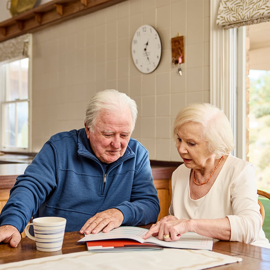 Two VMCH aged care residents sitting together at a table, reading documents and discussing plans over coffee at home.