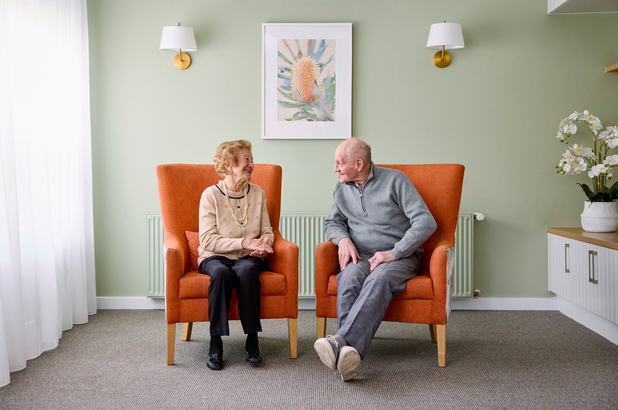 Female elderly resident and male elderly resident sitting next to each other in armchairs