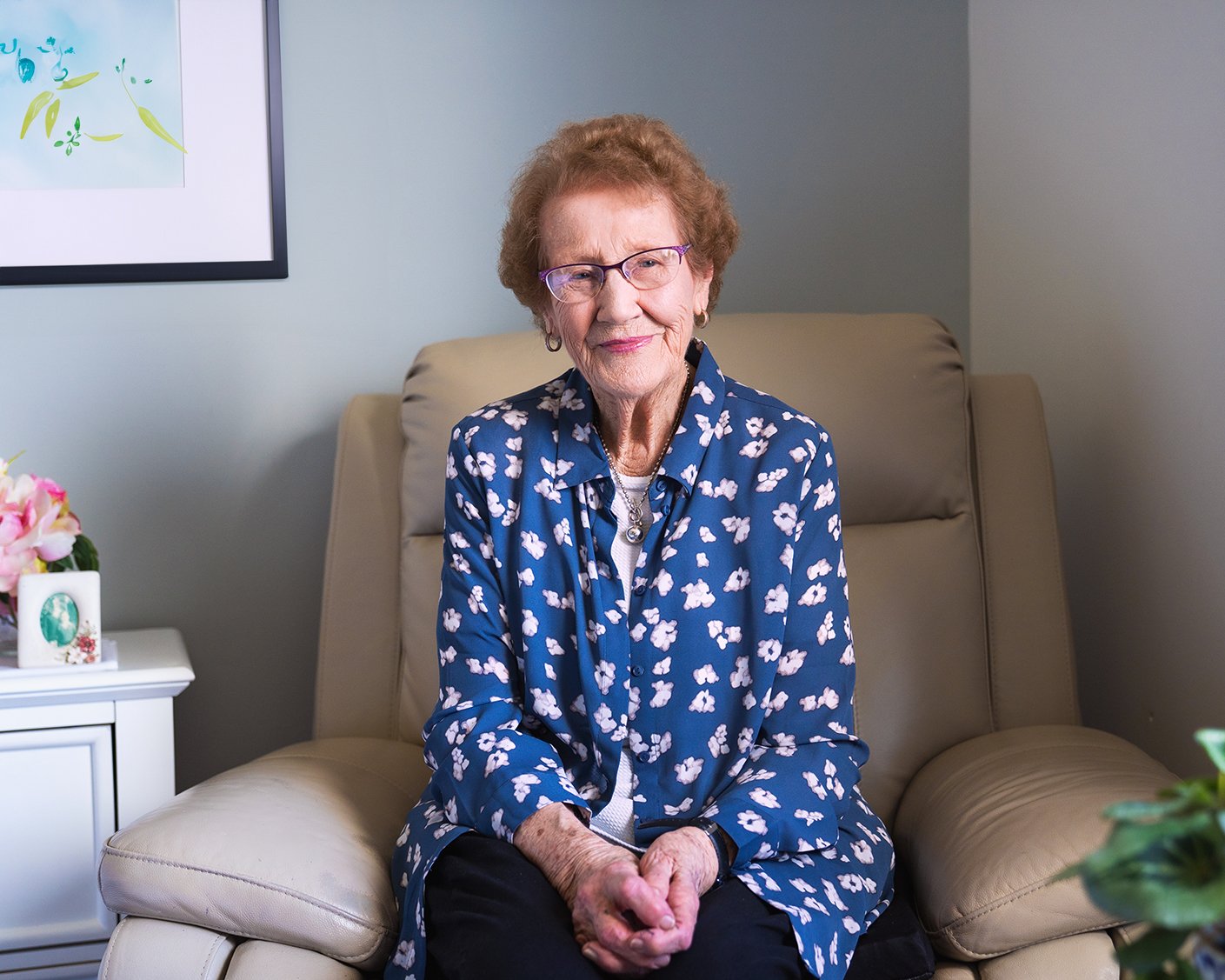 A woman in blue smiling in an armchair.