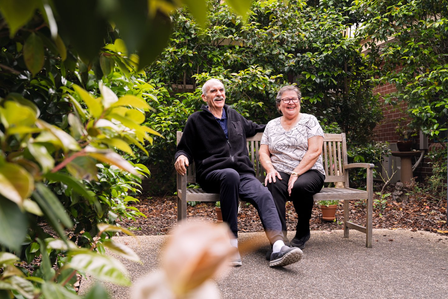 An older man and woman sitting outside on a bench seat laughing