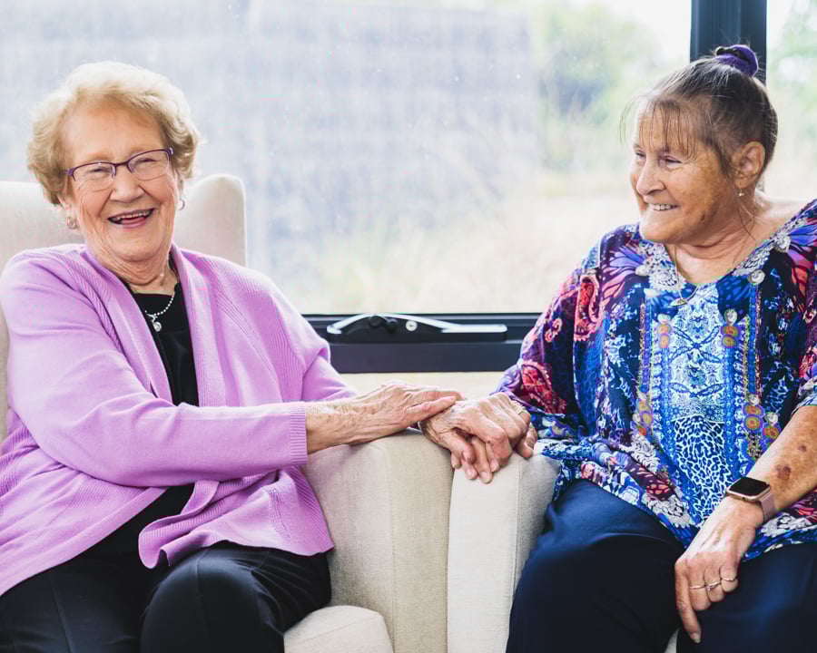 Two female elderly women sitting next to each other smiling and laughing