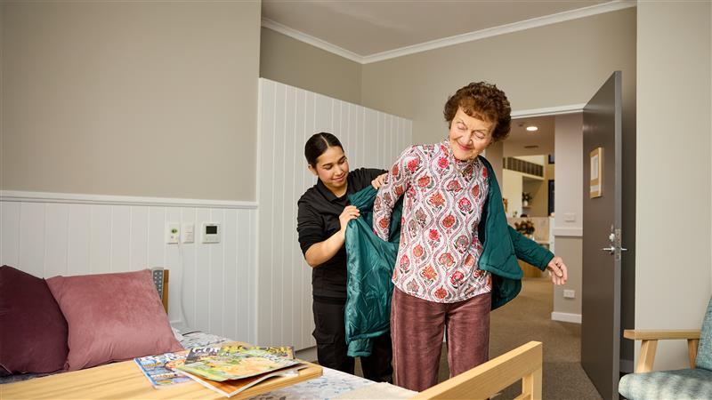 Aged care worker assisting resident getting dressed.